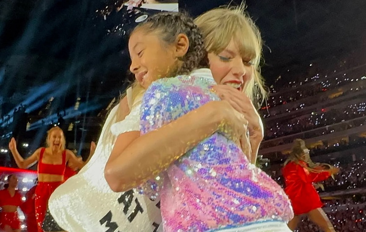 Taylor Swift trots up to a young fan belting out her song lyrics. After giving the girl a sweet hug, Swift hands her the coveted 22 trilby, causing the young fan to burst into happy tears.